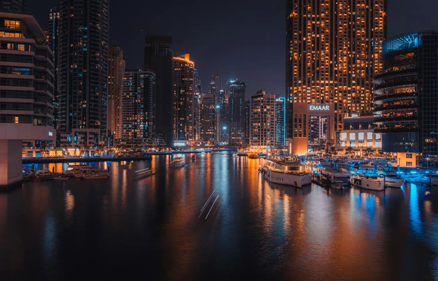 Dubai Marina skyline at night with illuminated skyscrapers and yachts along the waterfront.